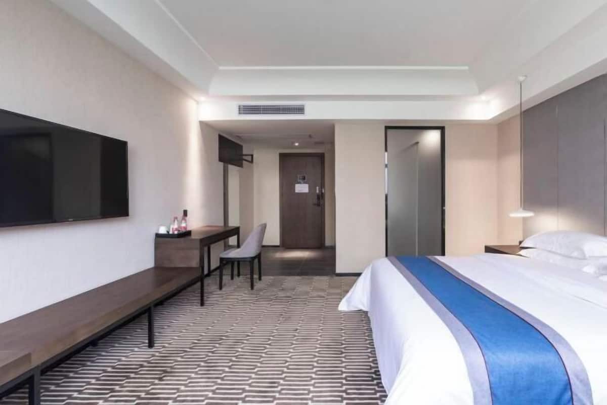A hotel room with a bed, a desk, a chair, a TV, and a door leading to a bathroom.