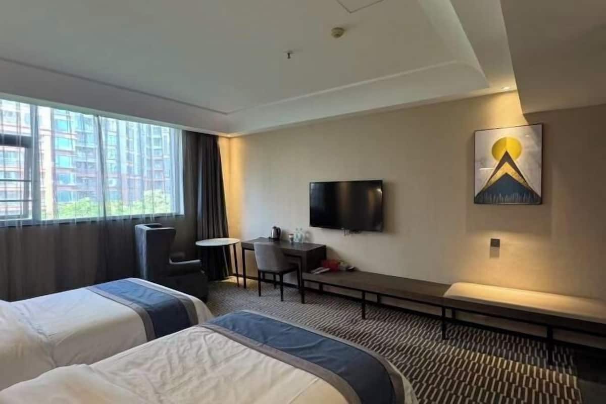 A hotel room with two beds, a desk, a chair, a TV, and a bench.