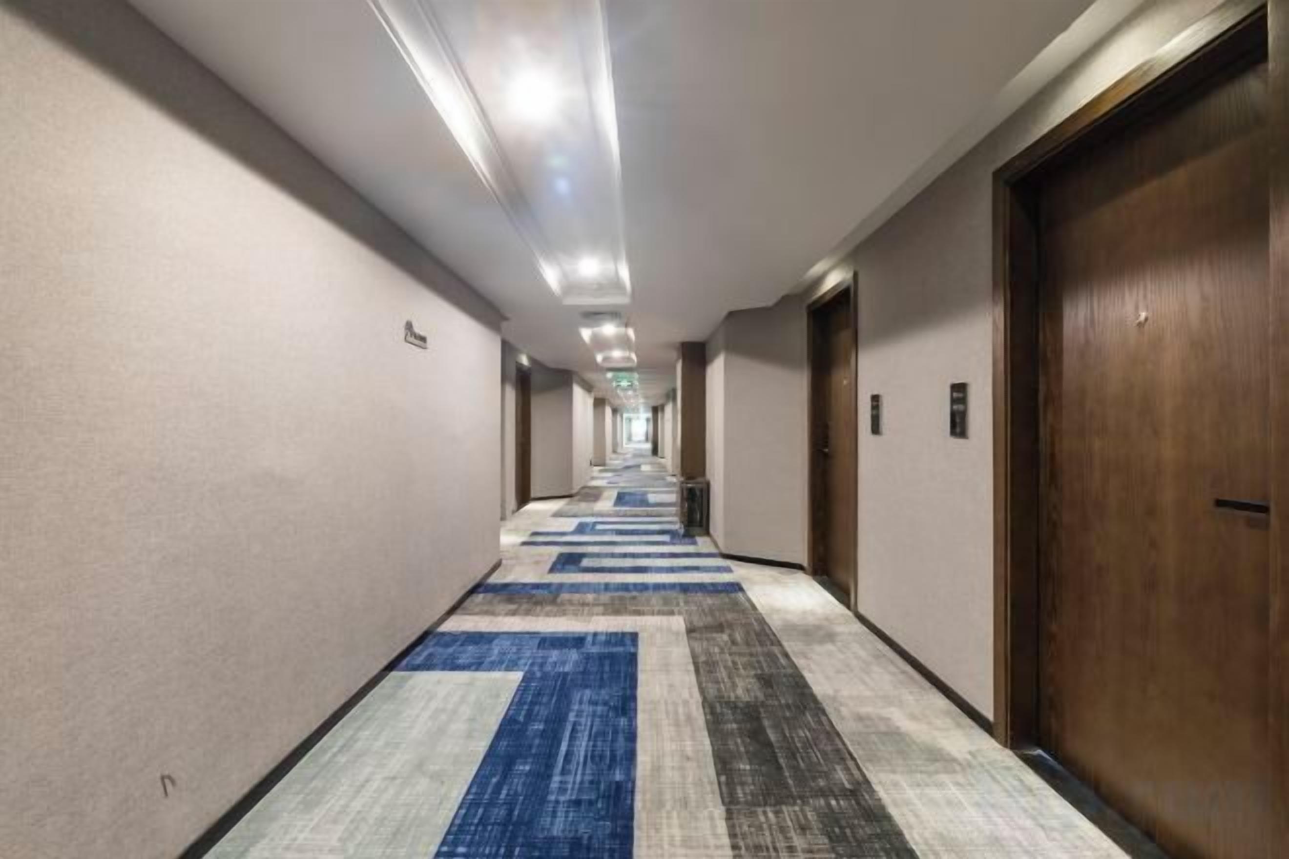 Un pasillo de hotel con suelo alfombrado, puertas a ambos lados e iluminación en el techo.