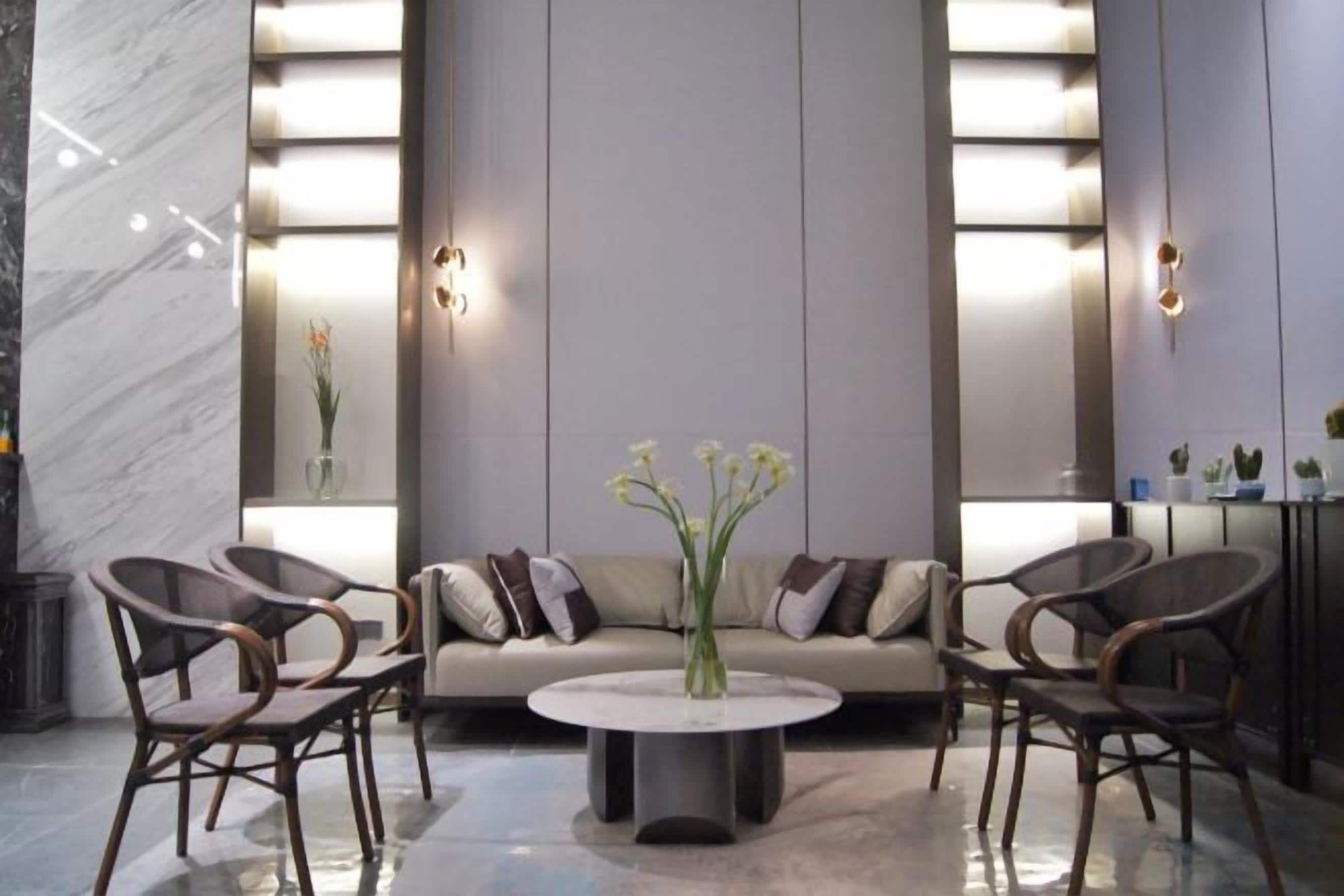 A modern lobby with a sofa, chairs, a round table, and a vase of flowers.