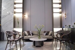 A modern lobby with a sofa, chairs, a round table, and a vase of flowers. - Duoman Hotel (Dongguan Xiping Metro Station) (Dongguan)
