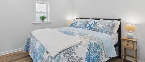 A bedroom with a bed, a nightstand, a lamp, a window, and a wall-mounted light fixture.