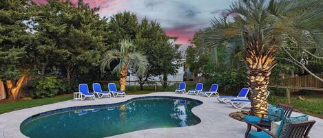 A swimming pool with blue lounge chairs and a palm tree.