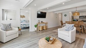 Una sala de estar moderna con sofás blancos, una mesa redonda y una zona de comedor con sillas y una mesa de madera.