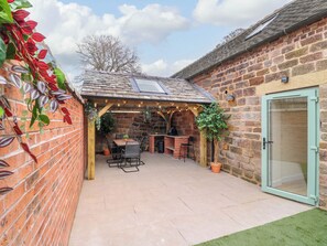 A patio area with a brick wall, a wooden pergola, a brick barbecue, and a seating arrangement. - The Long Barn (Stoke-on-Trent)