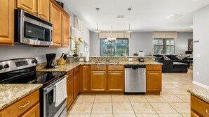A modern kitchen with granite countertops, wooden cabinets, stainless steel appliances, and a view to the living area.