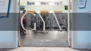 A gym entrance with a sign reading 'GYM' and a mat with 'Oasis Club' branding.