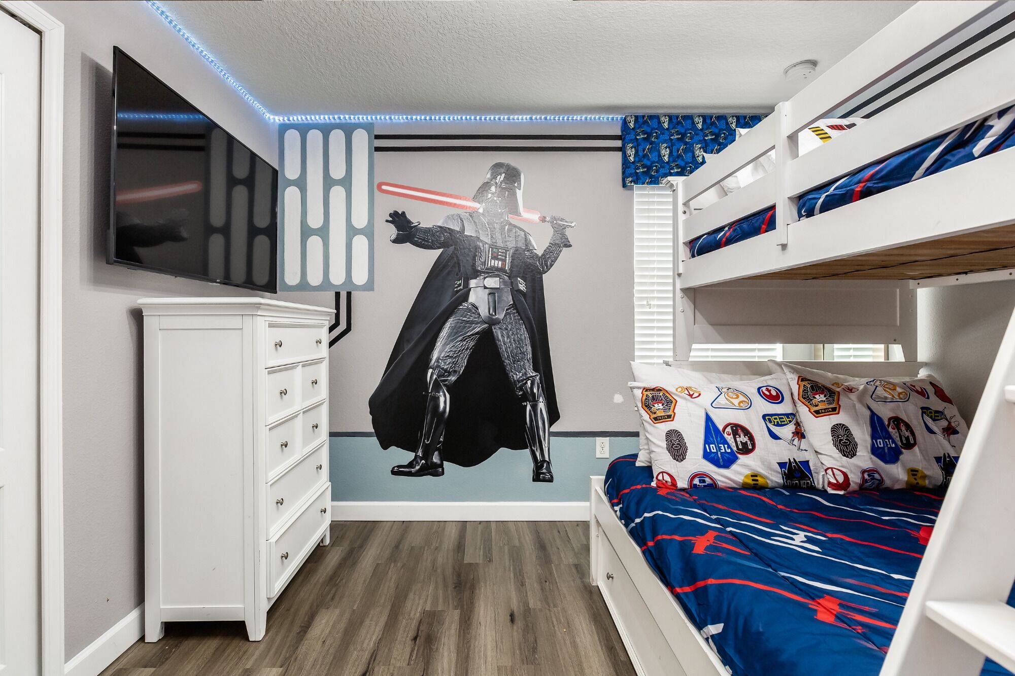 Un dormitorio con una pared temática de Star Wars, literas, un aparador y un televisor.