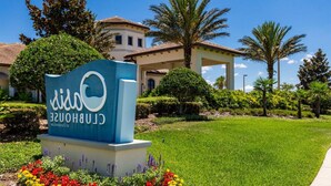 A sign for Clubhouse Resort with a well-maintained lawn and palm trees.