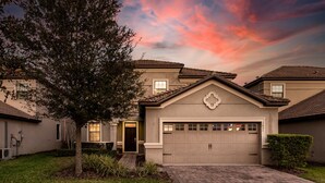 A residential house with a garage, a tree in the front yard, and a brick driveway.