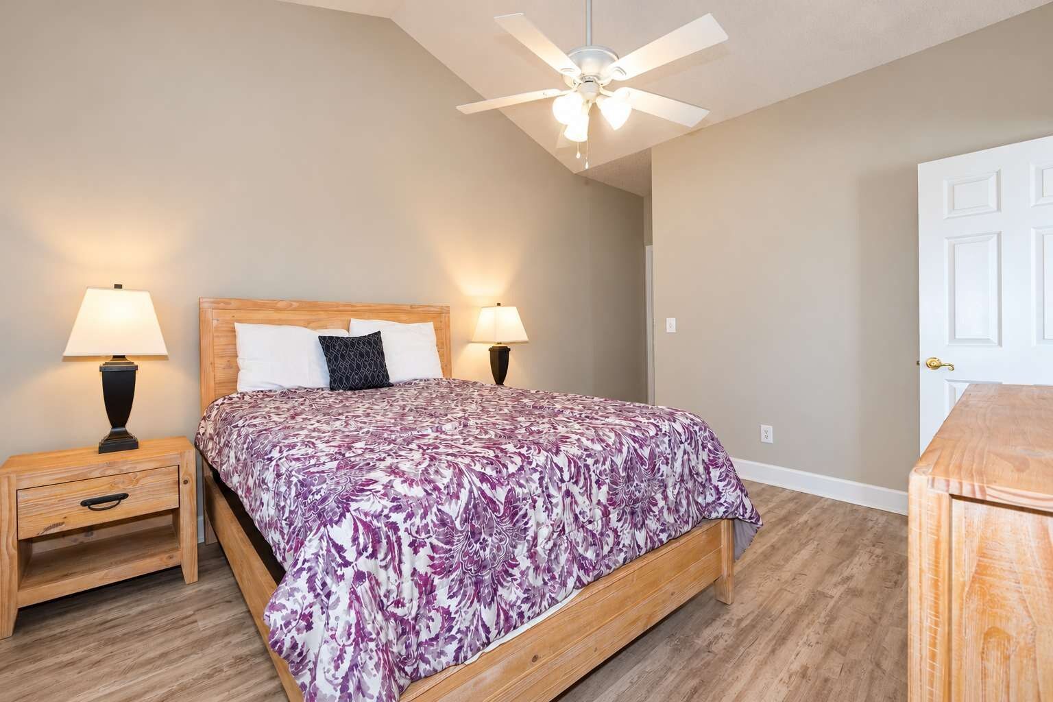 A bedroom with a bed, two bedside tables, a ceiling fan, and a door.