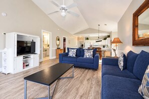 A spacious living area with a television, sofas, and a dining area in the background.
