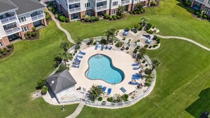 An aerial view of a hotel with a central swimming pool surrounded by lounge chairs and palm trees. - Spacious Condo, Private Balcony, Pool, Golf (Myrtle Beach)
