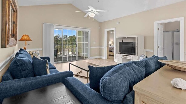 A spacious living room with a large sofa, a television, and a ceiling fan. - Spacious Condo, Private Balcony, Pool, Golf (Myrtle Beach)