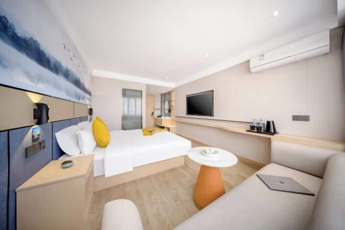A modern hotel room with a bed, a sofa, a small table, a TV, and a painting on the wall.