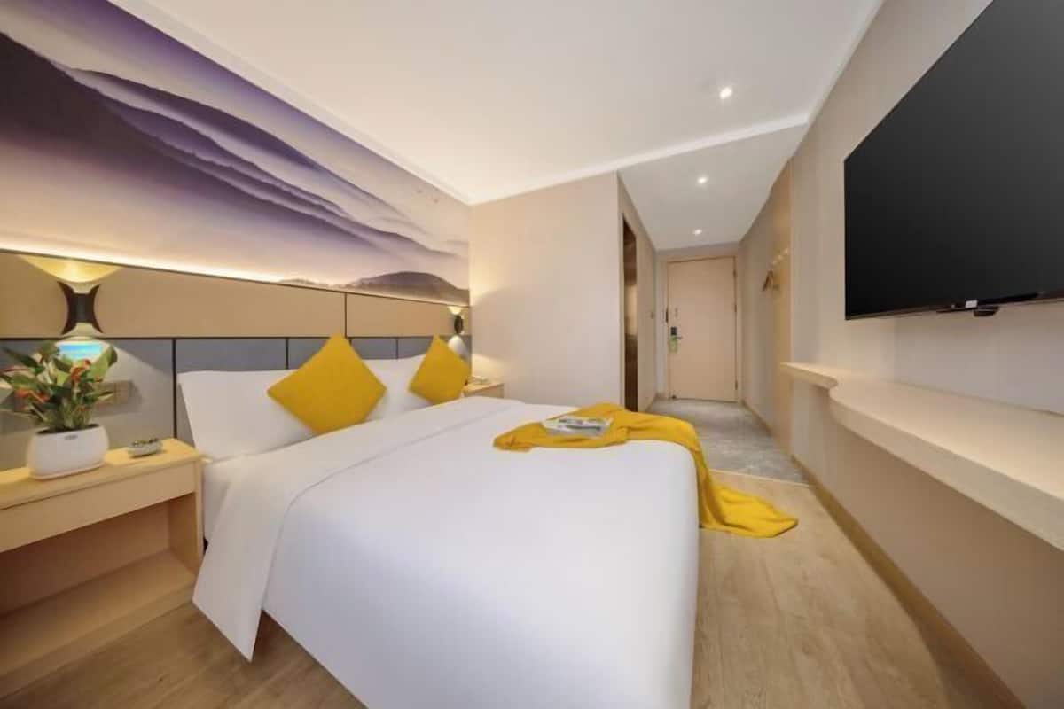 A modern hotel room with a bed, bedside table, lamp, and a flat-screen TV.