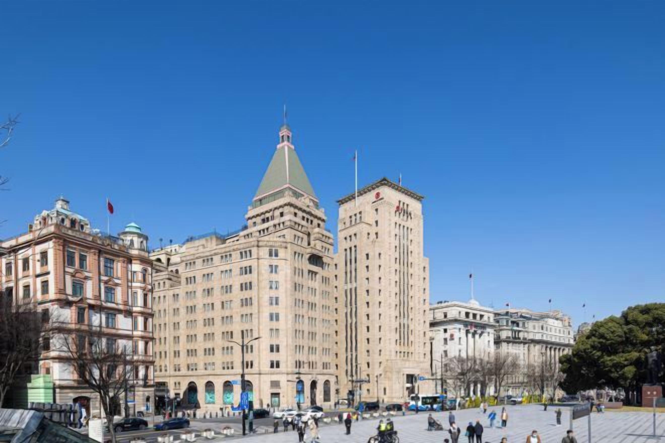 Un edificio grande con una torre destacada y una cúpula, rodeado por una plaza con gente y vehículos.