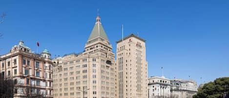 A large building with a prominent tower and a dome, surrounded by a plaza with people and vehicles.