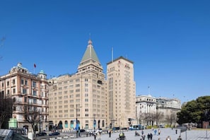 Ein großes Gebäude mit einem markanten Turm und einer Kuppel, umgeben von einem Platz mit Menschen und Fahrzeugen.