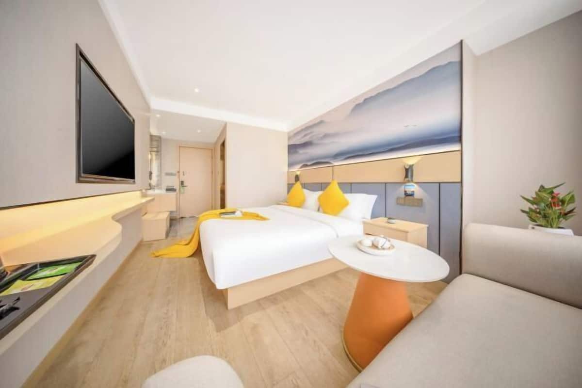 A modern hotel room with a bed, bedside table, TV, and a view of the sky.