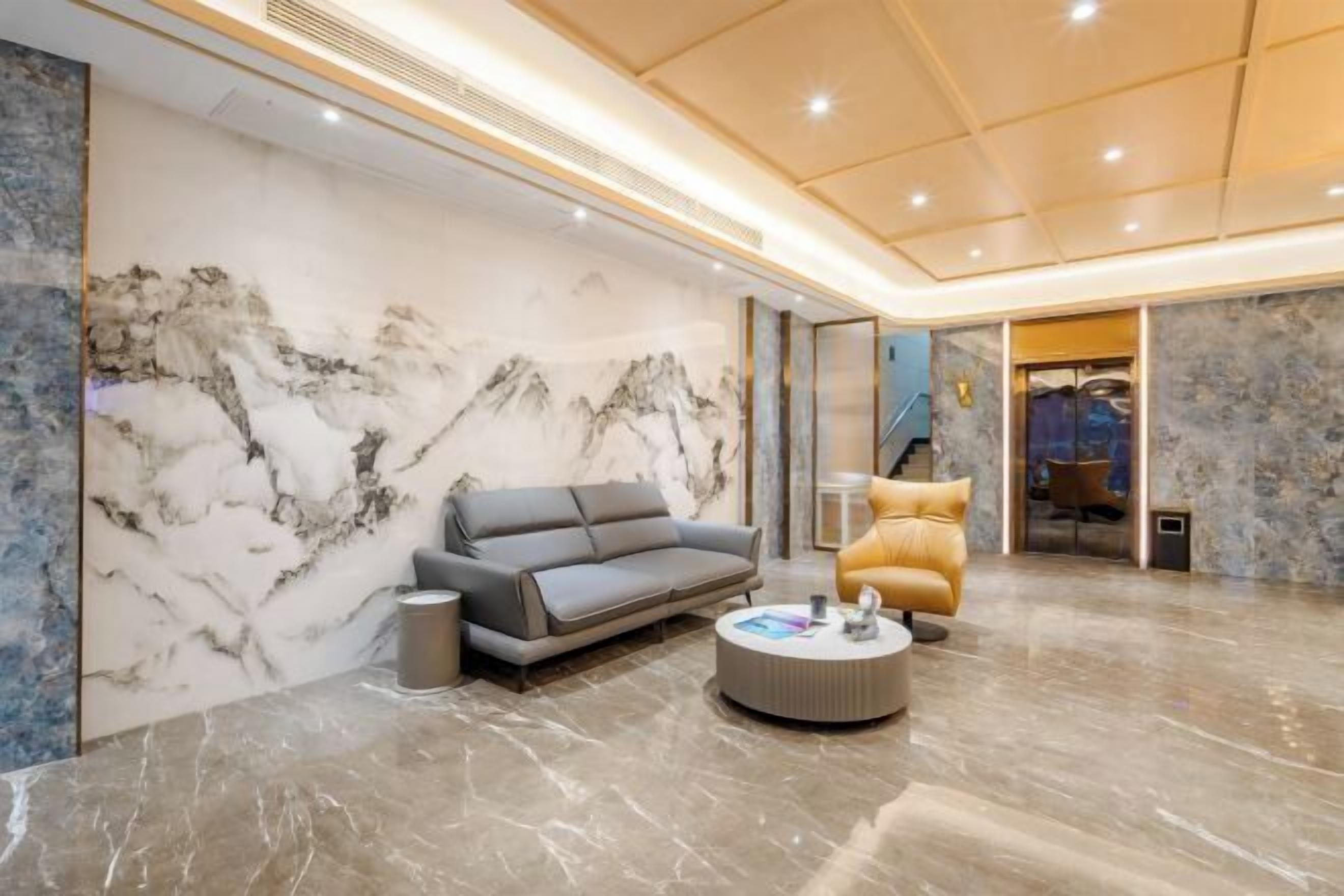 A modern interior with a marble wall, a grey sofa, a round coffee table, and a staircase leading to another room. - Yimi Collection Hotel (Shanghai Xizang North Road Subway Station) (Shanghai)