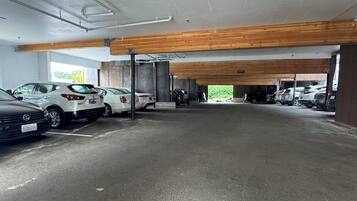 A parking garage with multiple cars parked, concrete floors, and wooden beams on the ceiling.