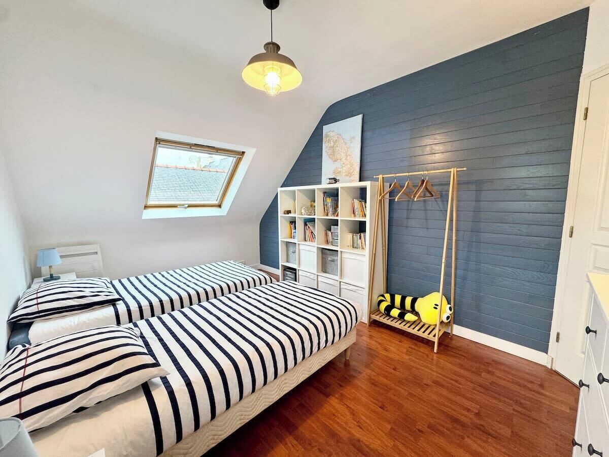 A bedroom with two beds, a bookshelf, a hanging rack, and a Minion plush toy.