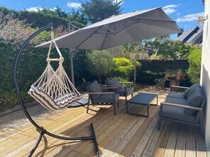 Um deck de madeira com mobiliário externo, incluindo uma cadeira suspensa e uma mesa.