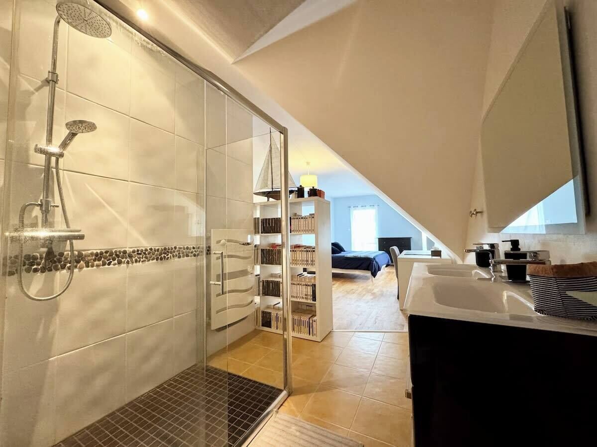 Une salle de bain moderne dotée d’une douche à parois de verre, d’une bibliothèque intégrée et d’une grande fenêtre laissant entrer la lumière naturelle.