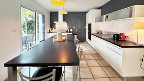A modern kitchen with a central island, white cabinets, and a black countertop. There are pendant lights above the island, and a window with a view of palm trees.