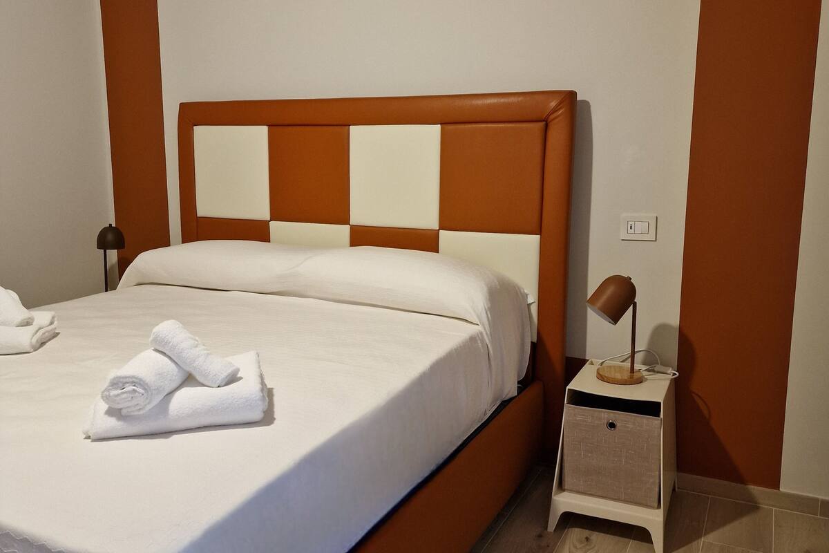 A neatly made bed with white linens and towels, a wooden nightstand with a lamp, and a brown accent wall.