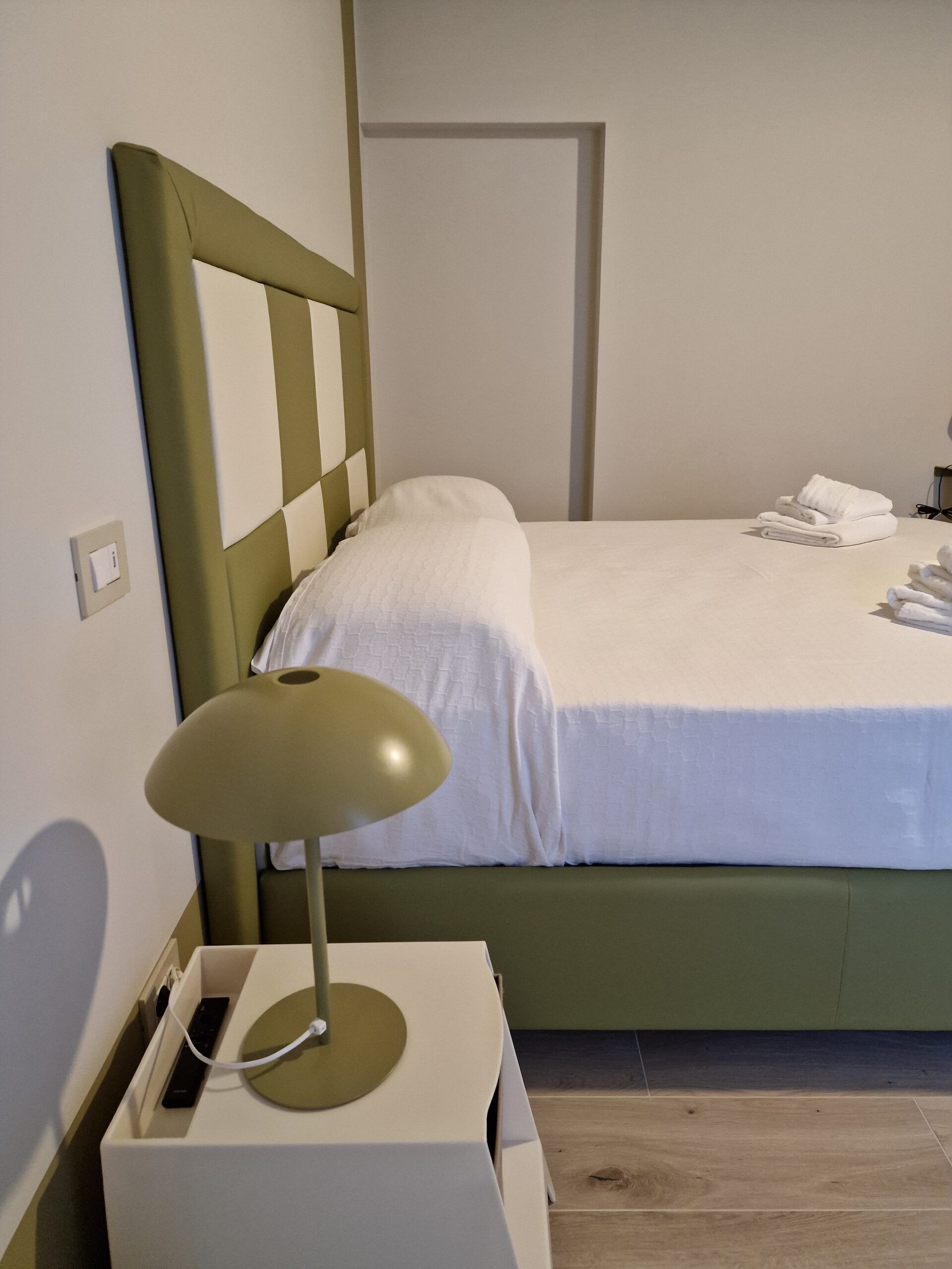 A neatly made bed with white linens, a bedside lamp, and a folded towel on the nightstand.