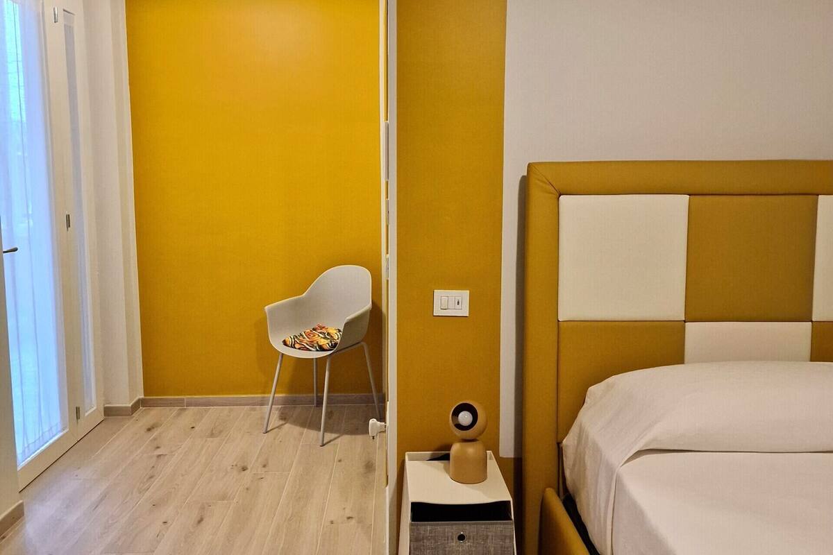 A room with a bed, a chair, a nightstand, and a wall-mounted light fixture.