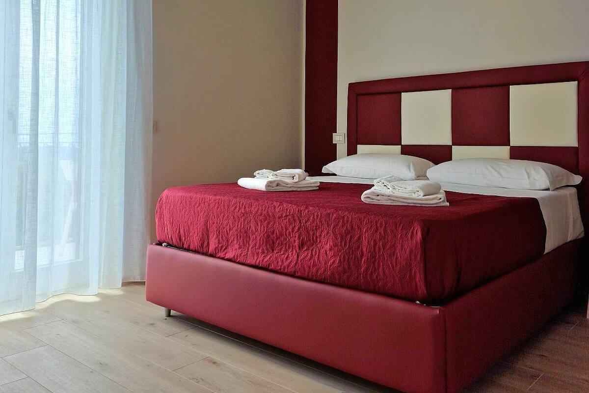A modern hotel room with a large bed, a red headboard, and a ceiling light.