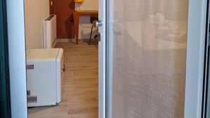A room with a white refrigerator, a small table with a lamp, and a wooden floor. - marte rooms (San Nicola)