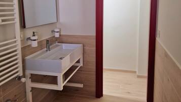 A bathroom with a double sink, a mirror, a toilet, and a red-framed door.