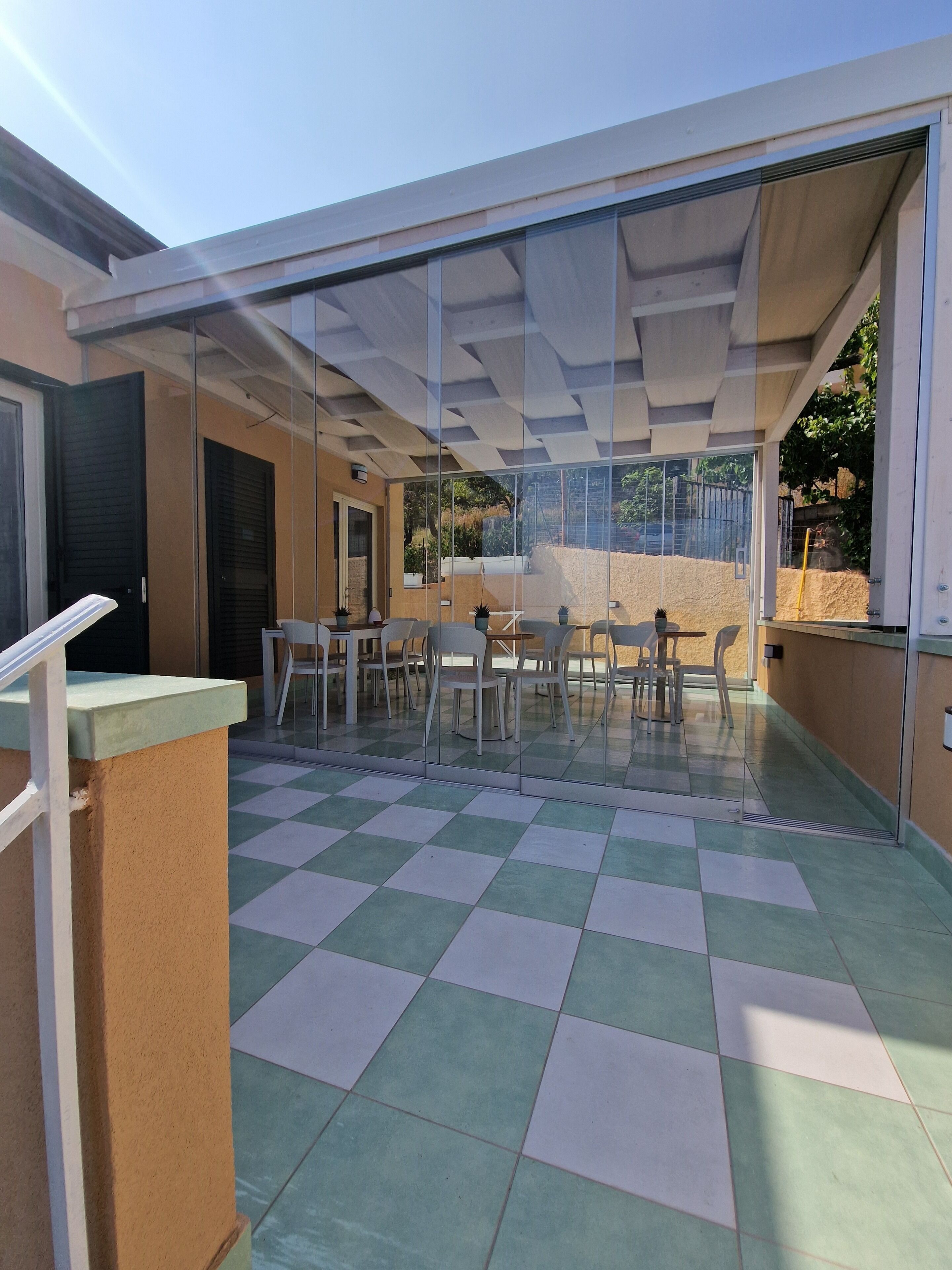 An outdoor patio with a checkered floor, a glass enclosure, and a seating area with tables and chairs.