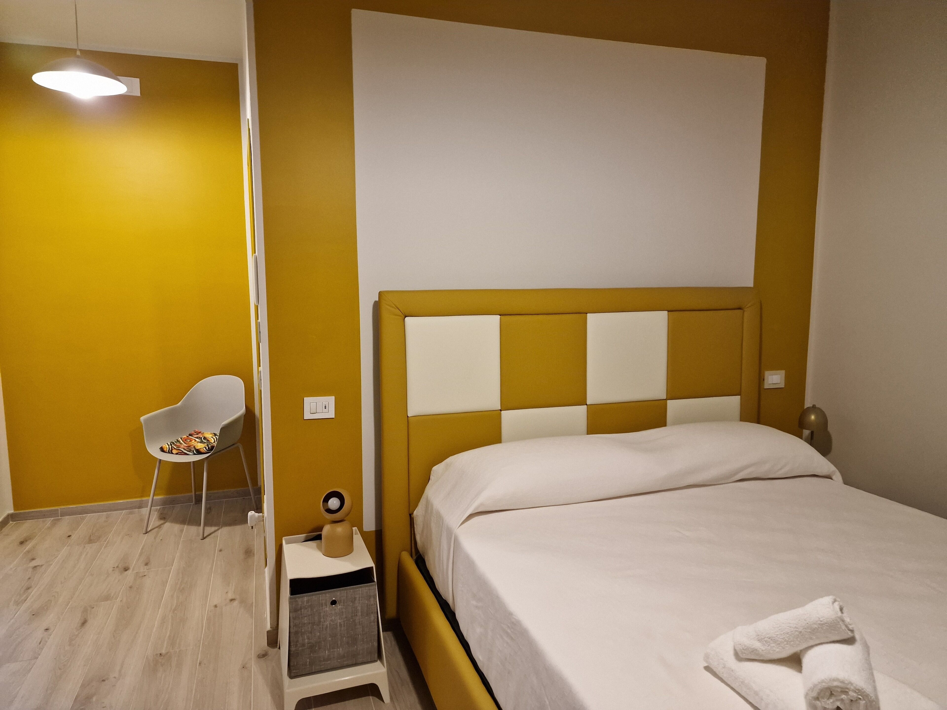 Una habitación de hotel con cama, mesita de noche, una silla y una lámpara fijada a la pared.