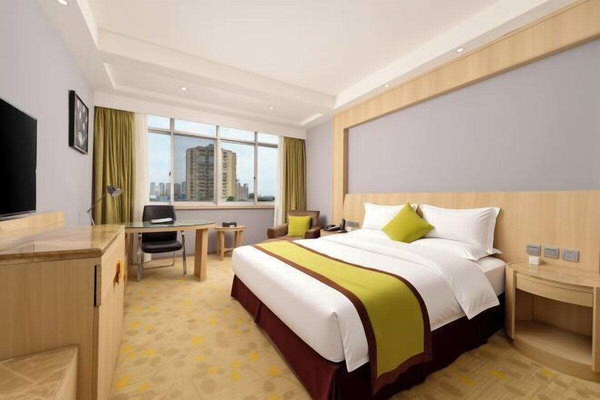 A hotel room with a bed, desk, chair, and a city view.