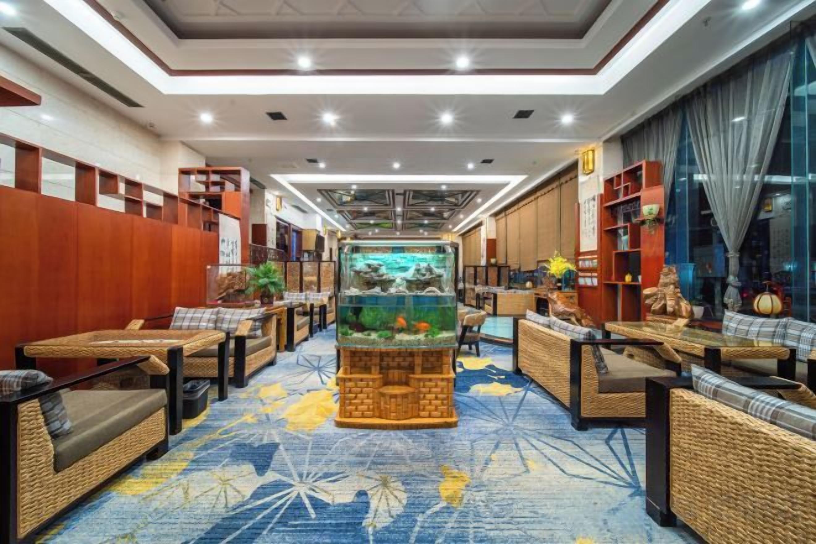 A hotel lobby with a central aquarium, seating areas, and a patterned carpet.