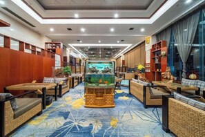 Eine Hotelhalle mit einem zentralen Aquarium, Sitzbereichen und einem gemusterten Teppich.