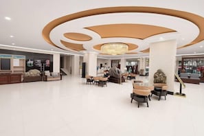 A spacious lobby with a modern chandelier, seating areas, and a staircase.