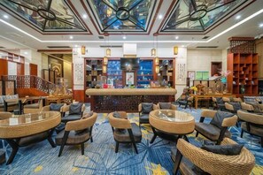 Een hotellobby met rieten meubels, een bar en een plafond met een glas-in-lood ontwerp.