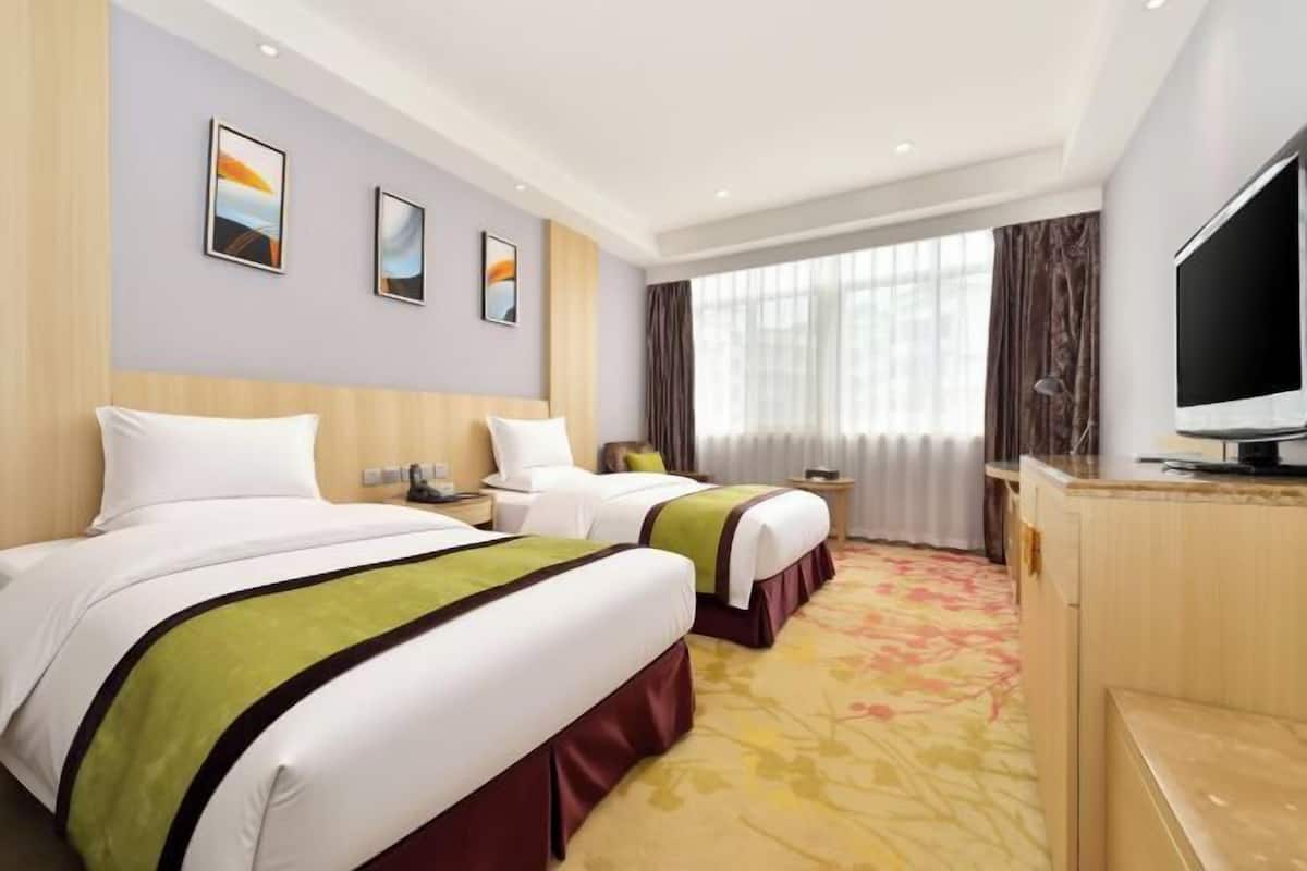 Habitación de hotel con dos camas, televisión, escritorio y un amplio ventanal con cortinas.
