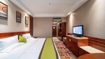 Quarto de hotel com uma cama, televisão, escrivaninha e porta que dá para outro espaço.