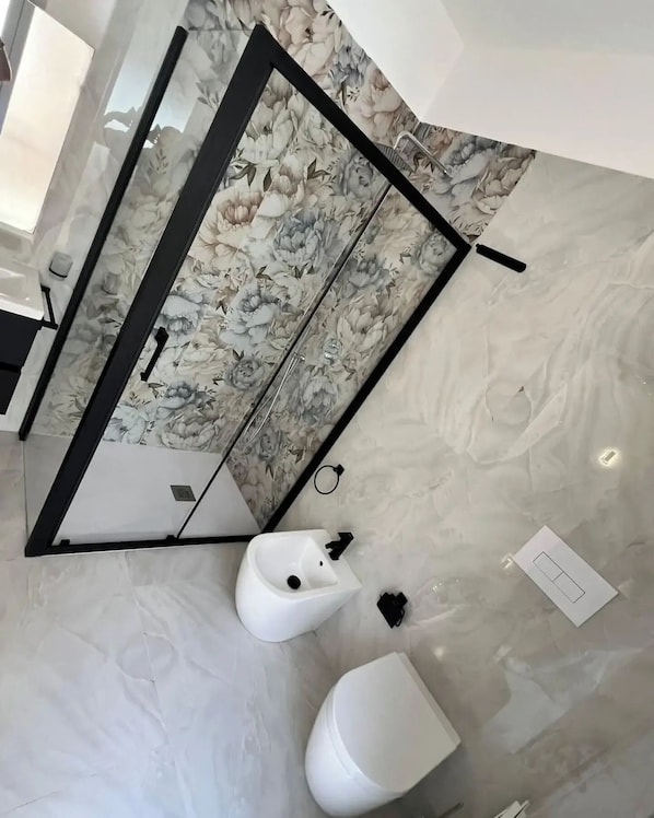 A bathroom with a marble floor, a bidet, a toilet, and a shower with a floral wallpaper. - Marisol (Palermo)