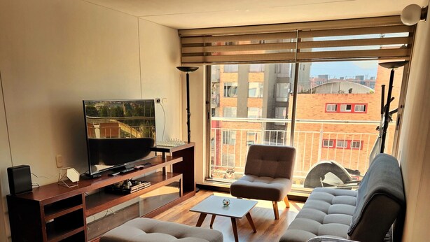 Una sala de estar moderna con una televisión de pantalla plana, piso de madera, un sofá, un reposapiés y una mesa de centro.