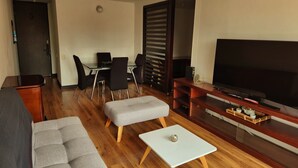 Una sala de estar moderna con sofá, reposapiés, mueble para televisión y un comedor con sillas y mesa.