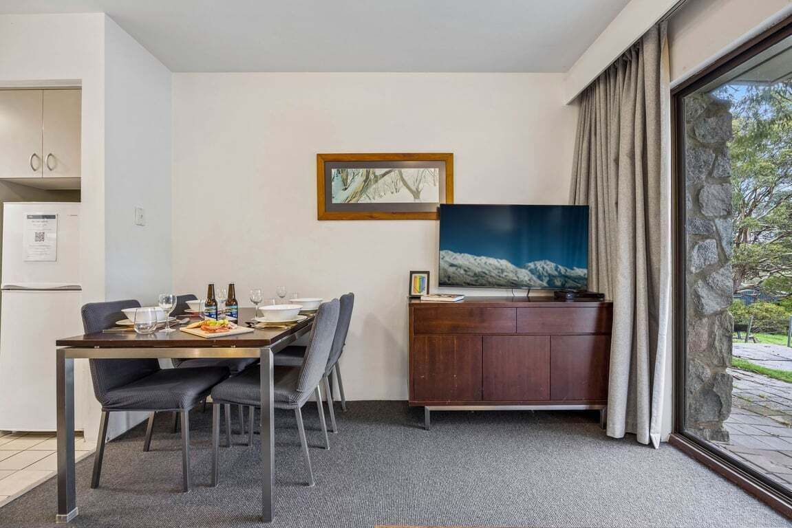 Una habitación de hotel moderna con comedor, televisor y pared de piedra.
