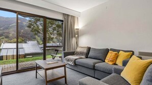 A modern living room with a grey sofa, a wooden coffee table, and a view of a mountainous landscape through large windows.